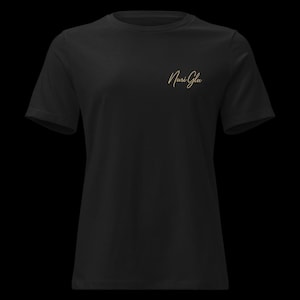 Könnte beinhalten: Schwarzes T-Shirt mit kurzen Ärmeln. Der goldfarbene Schriftzug "Nuri Glu" befindet sich auf der oberen linken Brust. Das Shirt besteht aus einem weichen Material und eignet sich für Freizeitkleidung.