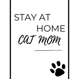 May include: A monochrome print featuring the text "STAY AT HOME cat mom". The words are in a mix of fonts, with a paw print at the bottom right. The print is framed in a black border.