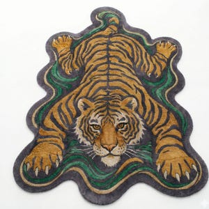 May include: A rug shaped like a tiger, featuring a detailed design. The rug has a brown and black striped pattern, with a green and gray border. The tiger's face is centered, with its paws extended.