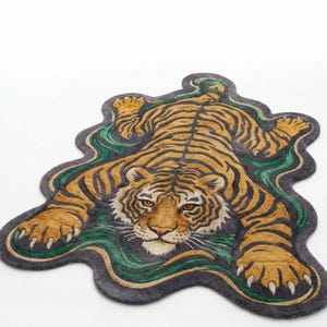 May include: A decorative rug in the shape of a tiger, featuring a detailed design with orange, black, and tan stripes. The rug has a dark gray border with green and tan wavy accents, creating a unique and artistic look.