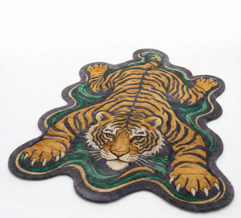 May include: A decorative rug in the shape of a tiger, featuring a detailed design with orange, black, and tan stripes. The rug has a dark gray border with green and tan wavy accents, creating a unique and artistic look.