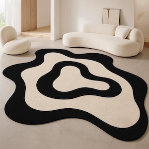 Puede incluir: Una alfombra moderna con un diseño abstracto en negro y crema. La alfombra presenta un patrón ondulado y orgánico. Se encuentra sobre un suelo embaldosado, con un sofá y una silla blancos al fondo, creando un ambiente minimalista.
