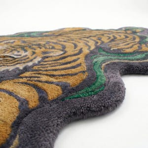 May include: A rug shaped like a tiger's head, featuring a detailed design. The rug has a gray border, with the tiger's fur in shades of gold and black. Green accents are also present in the design.