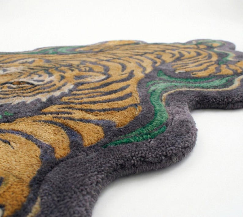 May include: A rug shaped like a tiger's head, featuring a detailed design. The rug has a gray border, with the tiger's fur in shades of gold and black. Green accents are also present in the design.