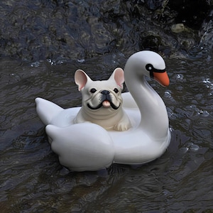 May include: A white French Bulldog figurine with black facial markings and a pink tongue, sitting inside a white swan-shaped float. The swan has a long neck, a black and orange beak, and is positioned in dark, rippling water with visible bubbles.