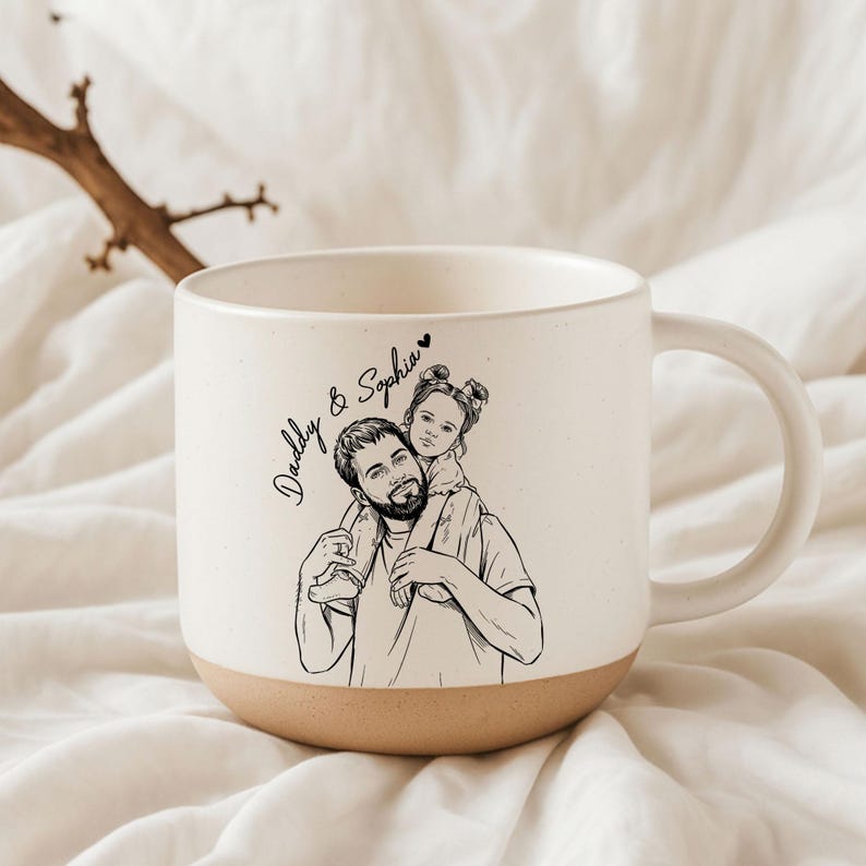 May include: Cream-colored ceramic mug with a tan base and a large handle. The mug features a black and white illustration of a father carrying a child on his shoulders, with the text "Daddy & Sophia".
