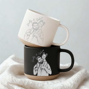 May include: Two ceramic mugs, one stacked on top of the other. The top mug is off-white with a tan base, and the bottom mug is black with a tan base. Each mug features a sketch of a father carrying a child on his shoulders, with the text "Daddy & Sophia".