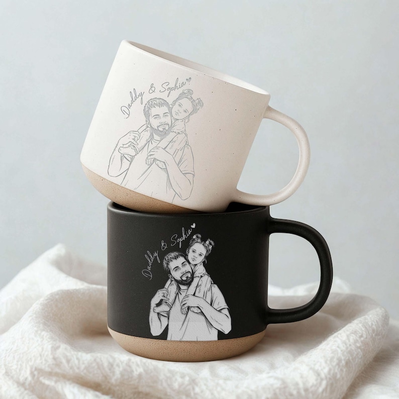 May include: Two ceramic mugs, one stacked on top of the other. The top mug is off-white with a tan base, and the bottom mug is black with a tan base. Each mug features a sketch of a father carrying a child on his shoulders, with the text "Daddy & Sophia".