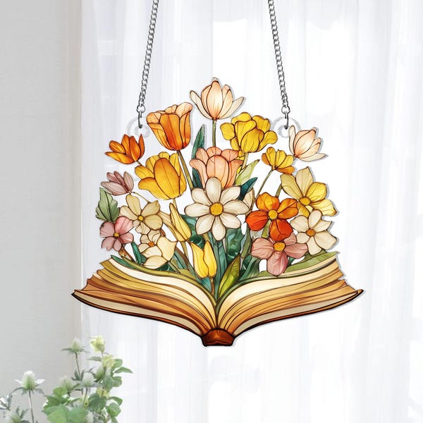 May include: A decorative hanging sign featuring a colorful floral arrangement emerging from an open book. The flowers include tulips, daisies, and other blooms in shades of yellow, orange, and pink. The sign is suspended by a silver chain.