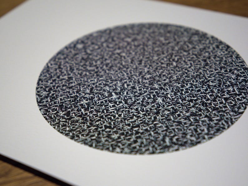 May include: A close-up of a circular design with a woven texture. The pattern is primarily black and white, creating a high-contrast visual effect. The design is centered on a white background.