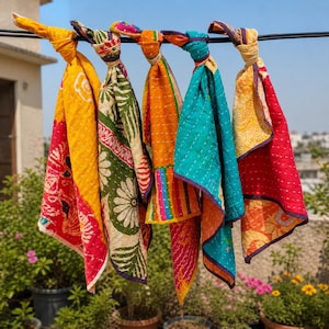 May include: Five rectangular fabric pieces with kantha stitching, each knotted at the top and hanging from a black wire. The textiles feature vibrant patterns in yellow, green, orange, teal, and red with floral and striped motifs throughout.
