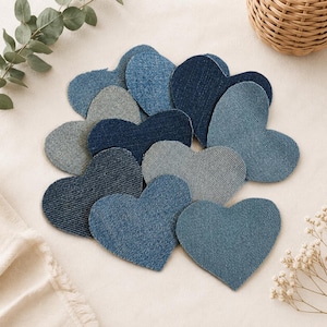 Puede incluir: Una colección de parches de tela con forma de corazón en varios tonos de mezclilla azul. Los parches presentan diferentes texturas y lavados, que van desde el índigo claro al oscuro, dispuestos en un grupo. Cada corazón es de mezclilla.