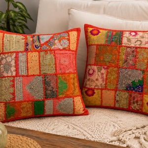 May include: Two square throw pillows featuring a patchwork design of various fabric rectangles in vibrant shades of red, orange, yellow, green, and pink. The pillows are accented with intricate embroidery, metallic thread detailing, and small mirrors.