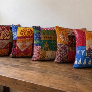 Puede incluir: Cinco cojines cuadrados con un diseño de patchwork de varias telas coloridas. Cada cojín muestra una combinación única de textiles rojos, amarillos, azules, verdes y naranjas con patrones intrincados, unidos por un acolchado de puntada recta visible.