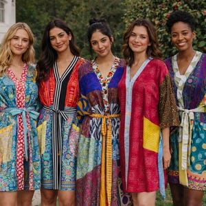 May include: Five women wearing colorful patterned robes. The robes feature a variety of patterns and colors, including blue, red, yellow, and green. Each robe has a belt or tie at the waist. The women are standing in front of a building and greenery.