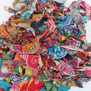 May include: A collection of vibrant fabric offcuts, featuring diverse patterns and textures. The scraps display shades of red, blue, yellow, and green, with visible stitching. The fabric seems to be repurposed, potentially from quilts or other textiles.