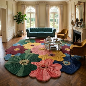 Op de afbeelding: Een groot, veelkleurig vloerkleed met een herhalend bloemenpatroon met extra grote, afgeronde bloemblaadjes in tinten donkergroen, koraal, geel, blauw en bordeauxrood. Elke bloem heeft een textuurrijk, verhoogd centrum voor een dimensionaal oppervlak.