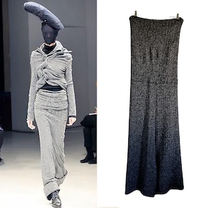 May include: A gray and black patterned skirt and top ensemble with a matching head covering. The outfit is worn by a person with a black face covering. The skirt is long and the top has a unique draped design.