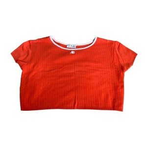 May include: A red ribbed crop top with a white trim around the neckline. The top has a small white bow in the center of the neckline.
