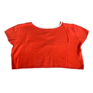 May include: A red ribbed crop top with a white trim around the neckline. The top has short sleeves.