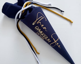 May include: A navy blue cone-shaped school bag with gold lettering that reads "Thea Gymnasium 2026 Fee". The bag has a drawstring closure with white, black, and gold cords.