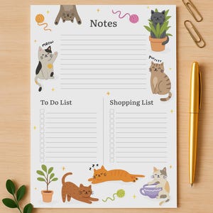 Puede incluir: Un bloc de notas con temática de gatos con secciones para notas, una lista de tareas y una lista de compras. El bloc de notas presenta ilustraciones de dibujos animados de gatos, ovillos de lana y plantas. Un bolígrafo dorado y clips están sobre la superficie de madera.