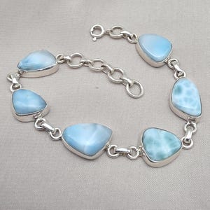 Peut inclure: Un bracelet en argent orné de sept pierres précieuses triangulaires bleu clair. Les pierres sont serties dans des chatons en argent et reliées par des maillons en chaîne argentée. Fermoir mousqueton.