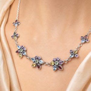 May include: A silver chain necklace featuring a series of floral-shaped links. Each link is composed of multiple teardrop and round-cut gemstones in various colors, including red, light blue, yellow, green, and purple, set in polished silver.