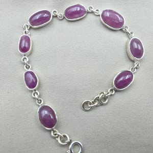Puede incluir: Una pulsera de cadena de plata con siete piedras cabujón ovaladas, lisas y de color magenta intenso, engastadas en biseles de plata individuales. La pulsera incluye un cierre de resorte circular y una cadena extensora con eslabones.