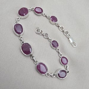 Könnte beinhalten: Ein silbernes Armband mit ovalen, tiefroten Edelsteinen. Die Edelsteine sind in einzelnen Silberfassungen gefasst und durch Silberglieder verbunden. Das Armband hat einen sicheren Verschluss. Der Schmuck wird auf neutralem Hintergrund präsentiert.