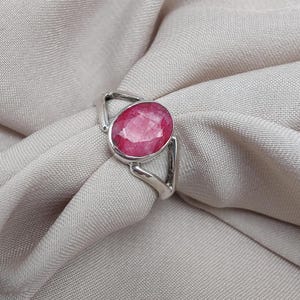 Peut inclure: Une bague en argent ornée d'une grosse pierre précieuse rose de forme ovale. La pierre précieuse est la pièce maîtresse, sertie dans un anneau en argent simple et moderne. La bague est présentée sur un tissu beige clair.