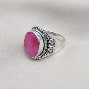 Può includere: Un anello in argento sterling con una grande gemma rosa brillante di forma ovale. L'anello presenta un'incastonatura ornata e dettagliata con un bordo di perline e dettagli decorativi. La fascia è liscia e lucida, mettendo in risalto il colore.