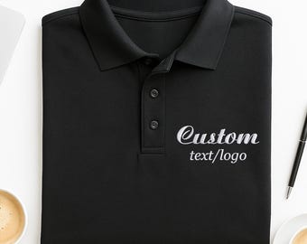 May include: Black polo shirt with a collar and three buttons. The shirt has the embroidered text "Custom text/logo" in white. The shirt is folded neatly on a white surface.