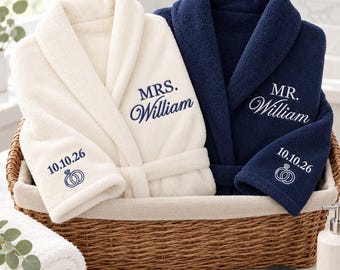 May include: A cream-colored bathrobe embroidered with 'MRS. William' and a navy blue bathrobe embroidered with 'MR. William'. Both robes feature the date '10.10.26' and an icon of two interlocking rings on the sleeve cuffs.