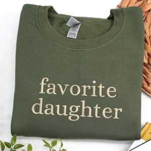 An military green sweatshirt embroidered with the phrase “favorite daughter” in a clean serif font.
The design is stitched in soft beige thread, creating a subtle and timeless contrast.
Minimal, cozy, and effortlessly stylish.