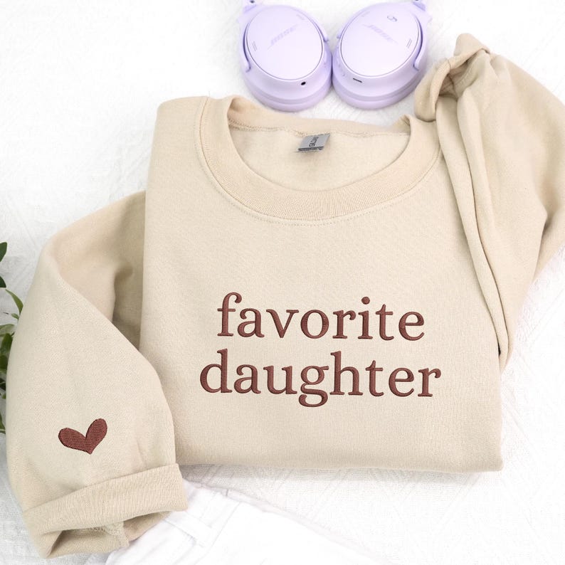 A neutral beige sweatshirt embroidered with the phrase “favorite daughter” in a warm brown thread.
A small heart detail on the sleeve adds a soft, thoughtful touch.
Simple, modern, and easy to style.