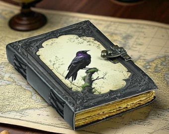 Può includere: Un diario in pelle nera con cornice e chiusura decorative. La copertina presenta un'illustrazione di un uccello nero con riflessi viola appollaiato su un ramo. Le pagine del diario hanno un aspetto vintage e invecchiato.
