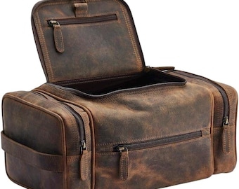 Peut inclure: Un sac de toilette en cuir marron avec plusieurs compartiments zippés. Le sac a une finition vieillie, lui donnant un aspect vintage. Le rabat supérieur est ouvert, révélant l'intérieur. Le sac a une poignée sur le côté pour faciliter le transport.