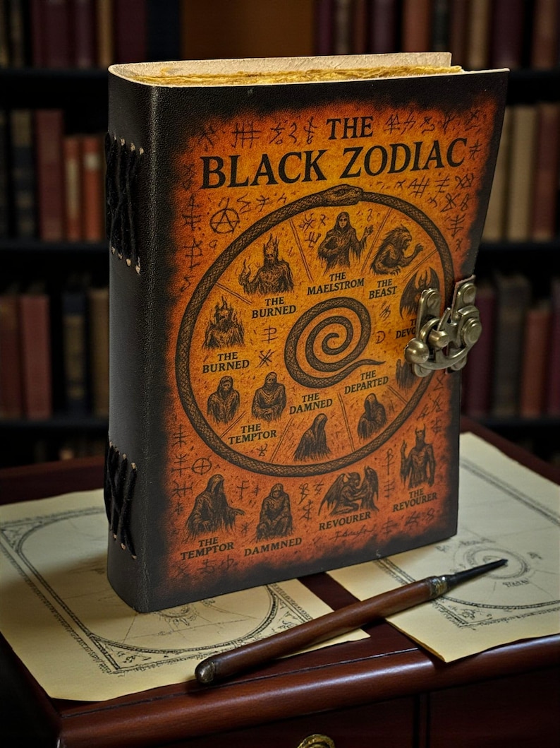May include: A leather-bound journal titled "The Black Zodiac" with an illustration of zodiac symbols. The cover has a clasp closure and is with a wooden pen. The journal is on a map.