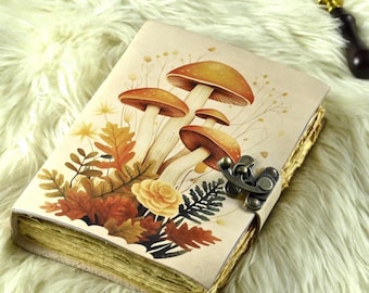 Peut inclure: Un journal de style vintage avec une illustration de champignons sur la couverture. L'illustration présente des champignons orange et bruns, des feuilles d'automne et une rose jaune. Le journal a un fermoir en métal et des pages en papier vieilli.