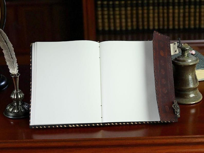 May include: An open, blank journal with a dark brown leather cover and a decorative clasp. A vintage inkwell with a feather quill and a small oil lamp sit nearby on a wooden surface, suggesting a writing or study theme.