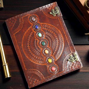May include: A brown leather journal with a decorative embossed design and a series of colorful gemstones. The journal features a metal clasp closure and intricate circular patterns.