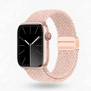 Może przedstawiać: Zegarek smartwatch w kolorze różowego złota z czarnym wyświetlaczem i białymi wskazówkami. Zegarek jest połączony z różowym, plecionym paskiem z zapięciem w kolorze różowego złota. Pasek ma subtelne plamki zieleni i innych kolorów.