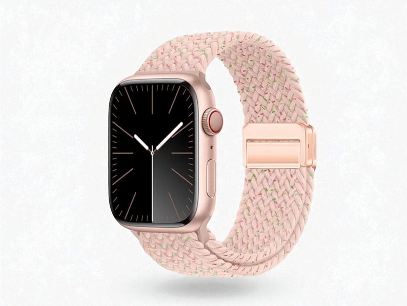 May include: A rose gold smartwatch with a black display and white hands. The watch is paired with a pink braided band with a rose gold clasp. The band has subtle flecks of green and other colors.