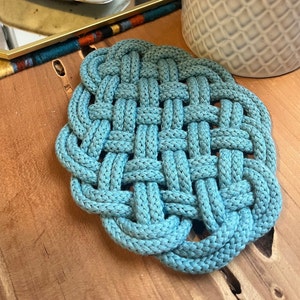 May include: A blue braided cotton trivet with a square pattern. The trivet is made of thick rope and has a woven design.