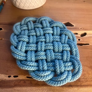 May include: A blue woven cotton coaster with a square shape and a knotted design.