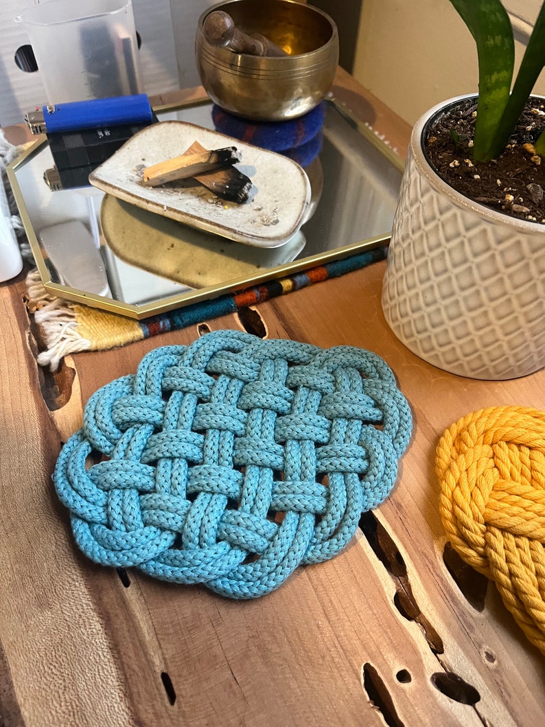 May include: Two woven rope trivets, one blue and one yellow, on a wooden surface.