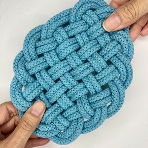 May include: A blue woven square coaster made from thick rope. The coaster is made with a knot pattern and has a slightly rounded shape.