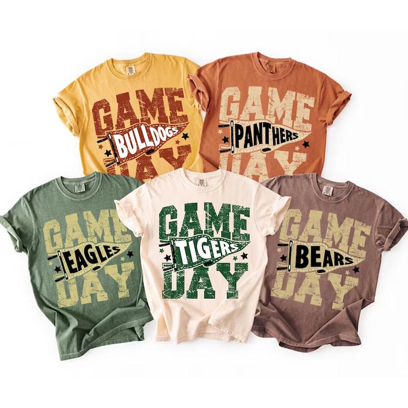 May include: Five short-sleeved t-shirts in various colors, each with a distressed graphic. The shirts feature the words "Game Day" above a team name, such as "Bulldogs," "Panthers," "Eagles," "Tigers," and "Bears." The text is in a collegiate style.