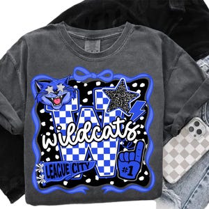 May include: A grey Wildcats sweatshirt featuring a blue and white graphic design. The graphic includes a cartoon cat, a star, and the words "Wildcats" and "League City". The design is outlined in blue and has a black and white polka dot background.